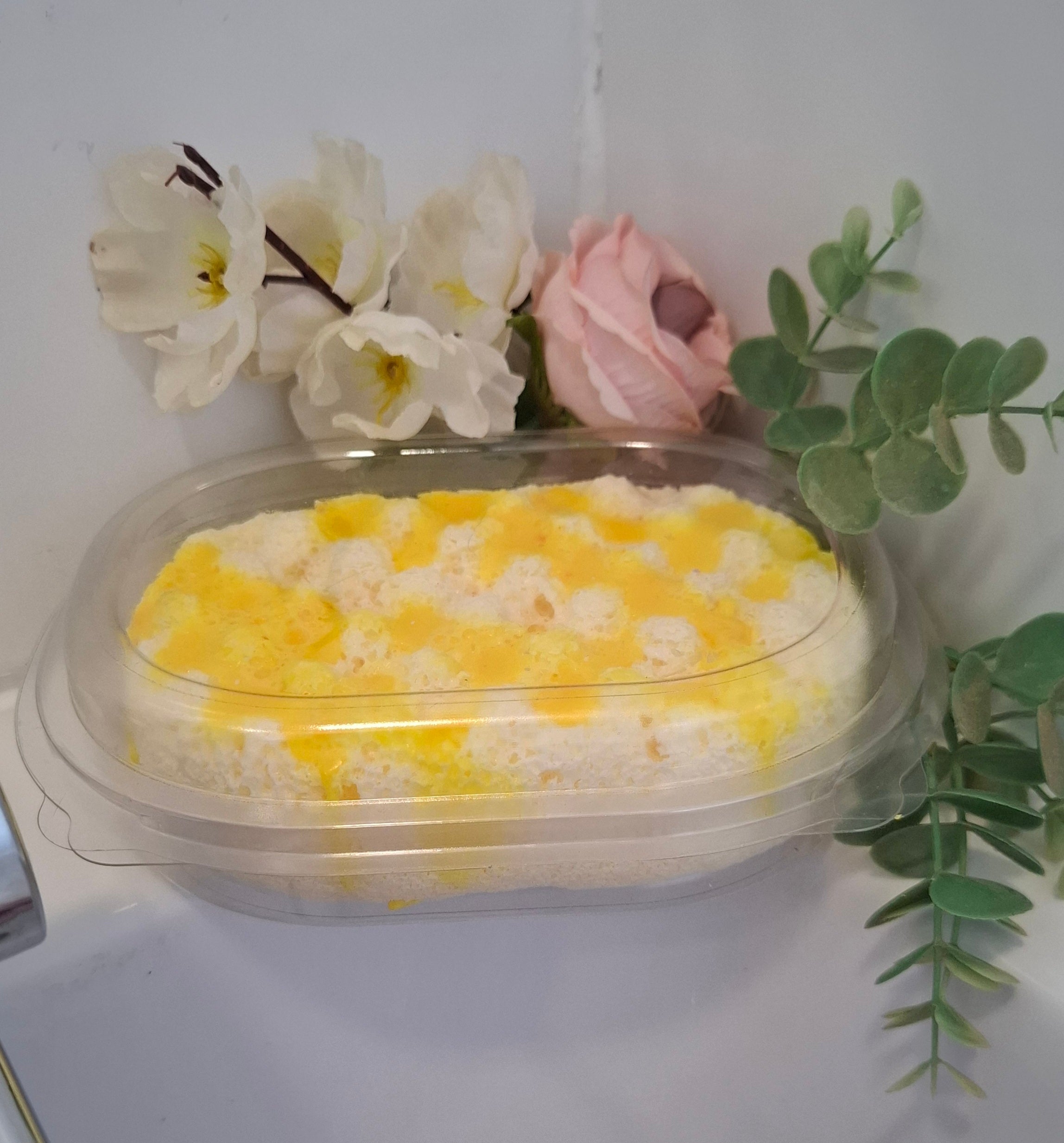lemon oval sponge with yellow drizzle poured over the top in plastic case to keep clean photo set on side of bath with tap and flowers in back ground